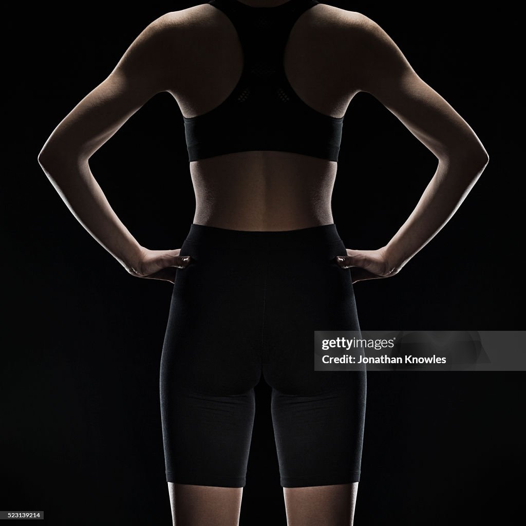 Mid section rear view of female wearing gym sports clothing, studio shot against black background