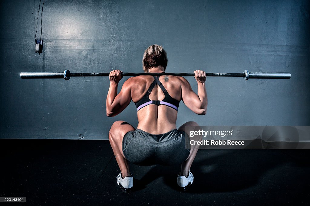 Woman in gym gym with weight bar on shoulders