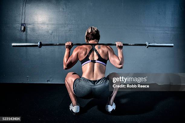 woman in gym gym with weight bar on shoulders - hockend stock-fotos und bilder