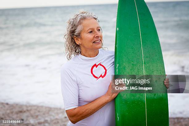 smiling woman holding surfboard on beach - older woman wet hair stock pictures, royalty-free photos & images