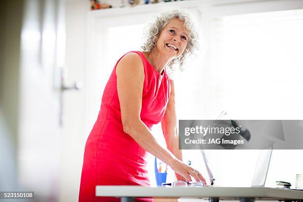 middle age woman working in her home office - red dress stock pictures, royalty-free photos & images