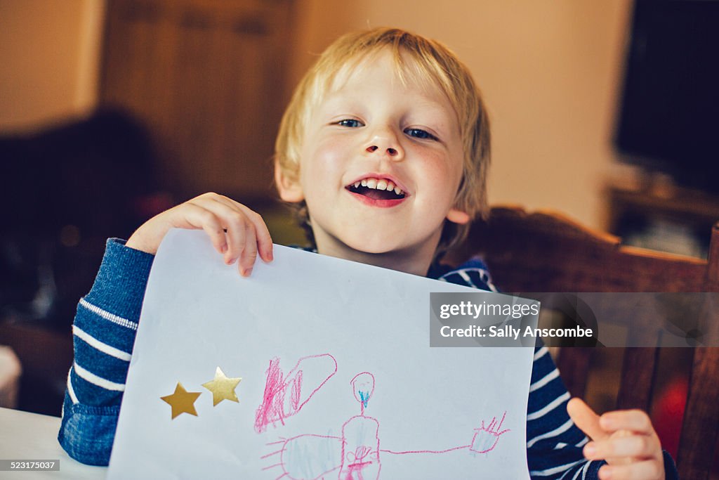 Smiling child holding up a picture he has drawn