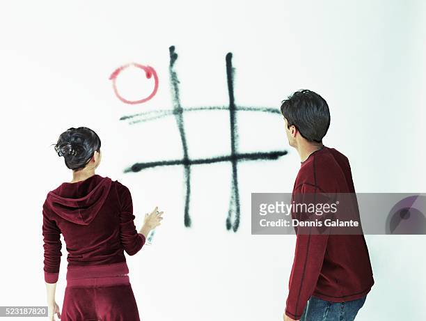 young couple spray painting tic-tac-toe on wall - tic tac toe stock-fotos und bilder
