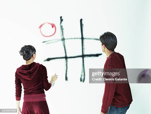 young couple spray painting tic-tac-toe on wall - tic tac toe stock pictures, royalty-free photos & images