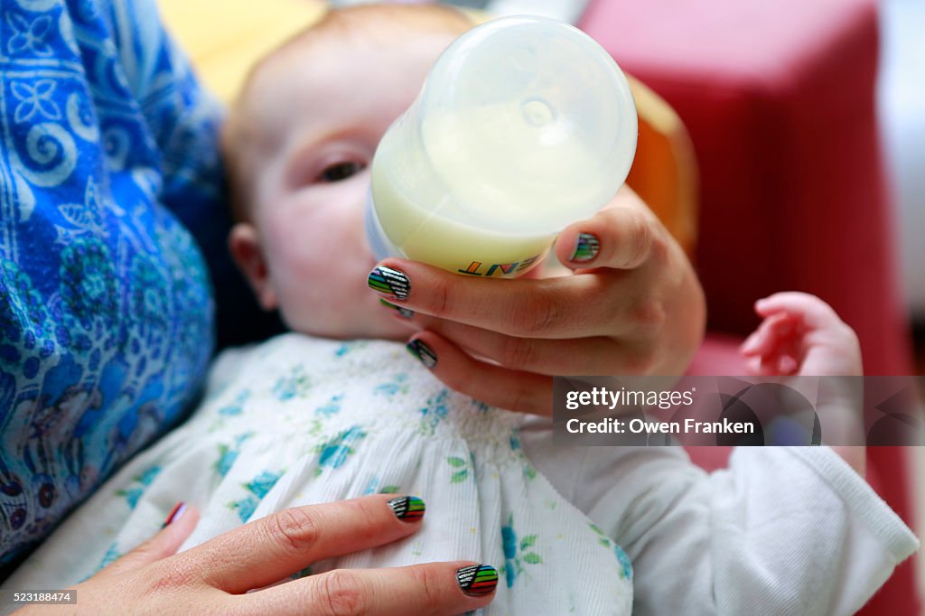 A nanny bottle feeding a bright-eyed six month old girl
