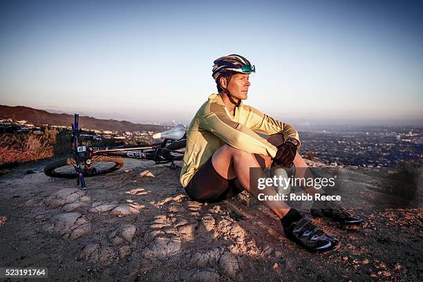 a male mountain bike rider sits and rests during a trail ride while overlooking a city - robb reece stock pictures, royalty-free photos & images