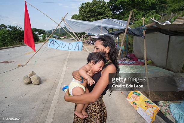 Woman carries a baby next to the highway after an earthquake struck Ecuador on April 21, 2016 in Pedernales, Ecuador. Some neighbours wait next to...