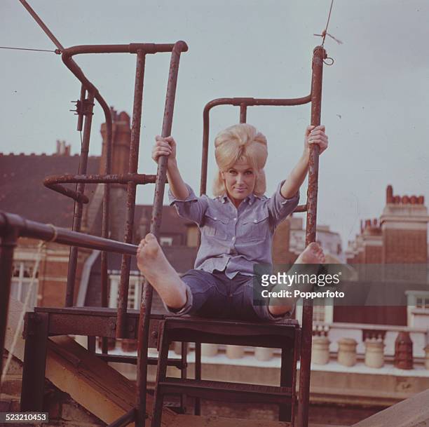 English singer Dusty Springfield pictured barefoot and wearing jeans and a blue shirt on a rooftop fire escape in London in 1963.