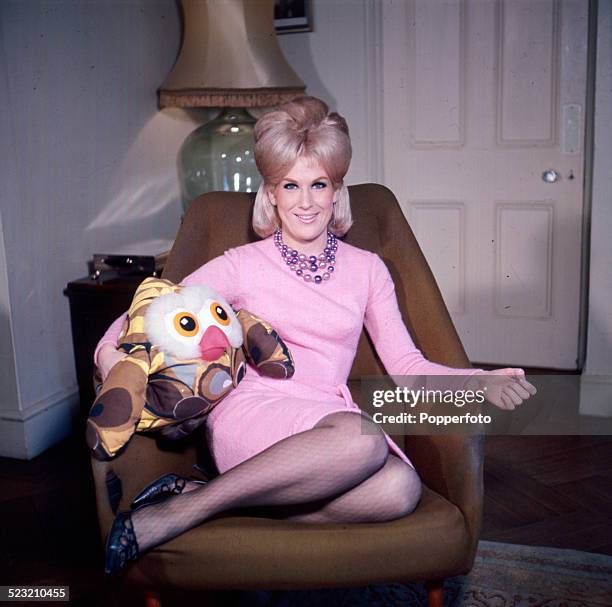 English singer Dusty Springfield posed sitting in a chair wearing a pink dress holding a cuddly toy owl in 1963.