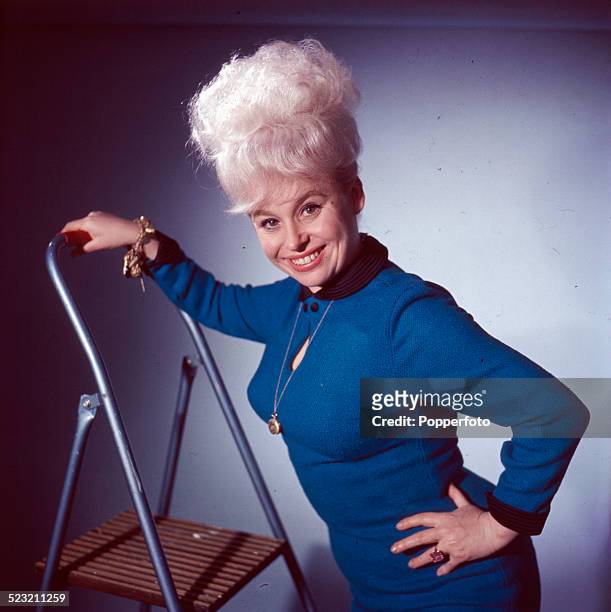 English actress Barbara Windsor posed wearing a blue dress whilst standing on a ladder in 1963.