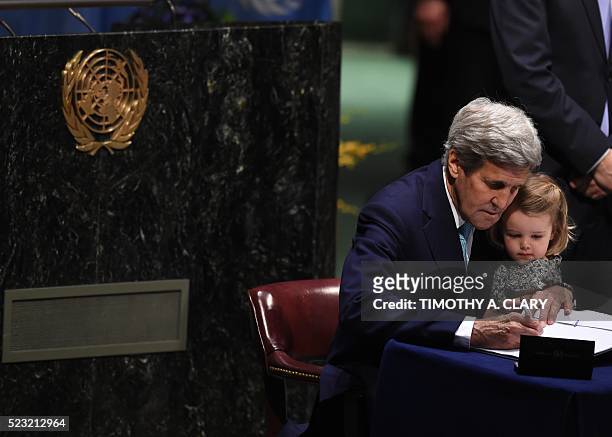 Secretary of State John Kerry signs the book holding his granddaughter, during the signature ceremony for the Paris Agreement at the United Nations...