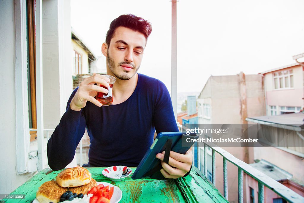 Handsome Turkish man enjoying media on his tablet during breakfast