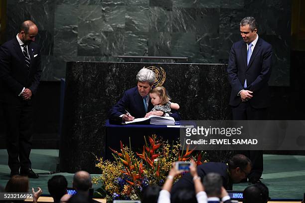 Secretary of State John Kerry signs the book holding his granddaughter, Isabelle Dobbs-Higginson, during the signature ceremony for the Paris...