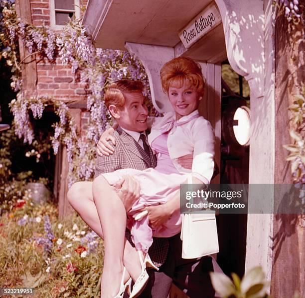 Scottish actor Stanley Baxter carries actress Sally Smith across the threshold of a cottage in a scene from the film Father Came Too! In 1963.