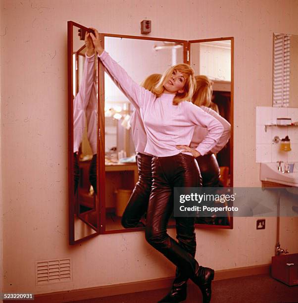 English actress Susan Hampshire posed wearing a pink top and leather trousers in front of a trio of mirrors in a dressing room in 1964.