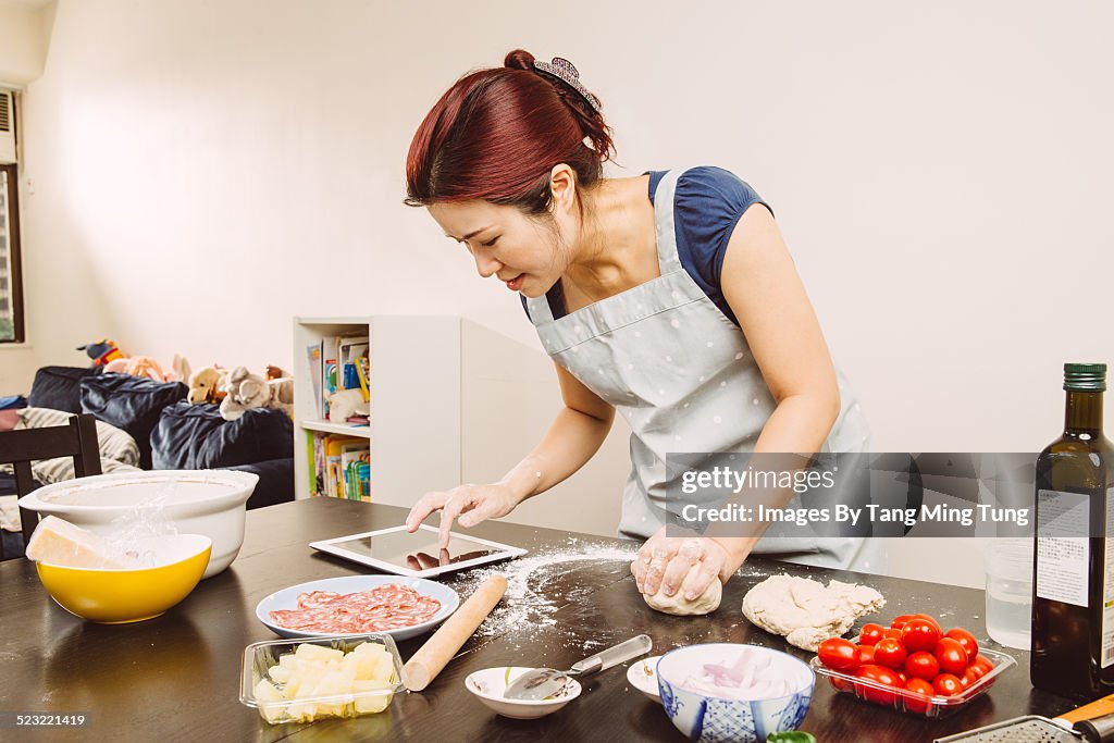 Young lady making pizza at home with tablet