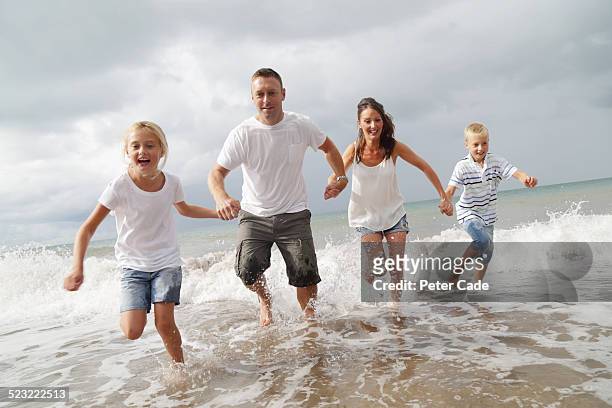 family on beach running trough  the waves . - run shirt stock-fotos und bilder