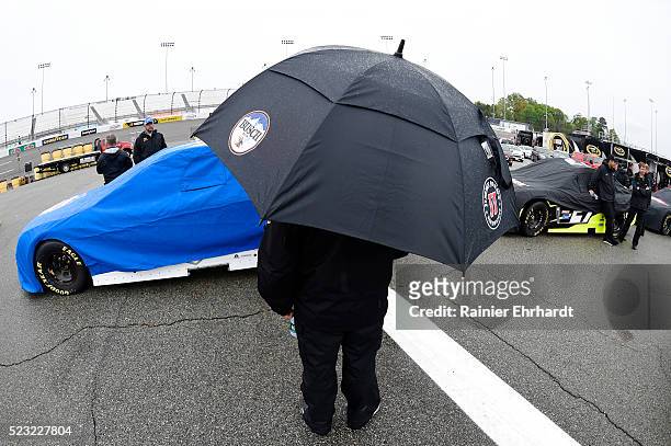 Crew member holds an umbrella in the garage area as it rains at Richmond International Raceway on April 22, 2016 in Richmond, Virginia.