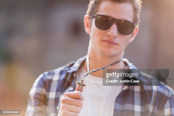 portrait of a young man showing his necklace with crucifix - a cross necklace stock-fotos und bilder