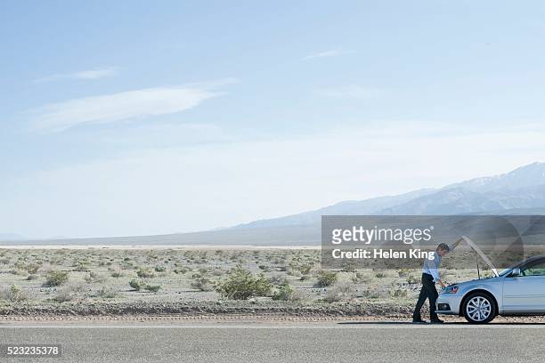 man with a broken down car in the desert - funktionsuntüchtig stock-fotos und bilder