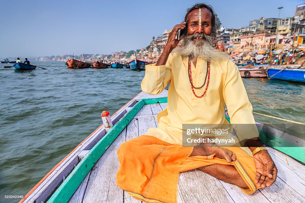 Sadhu using mobile in boat on Holy Ganges River, Varanasi