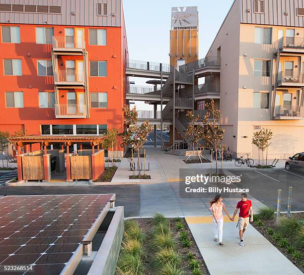 two persons walking near green buildings and solar panels, in a zero net energy community - billy walker stock pictures, royalty-free photos & images