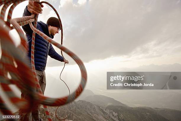 young man holding rope on rock in mountains, alps, tyrol, austria - tightrope walking stock-fotos und bilder