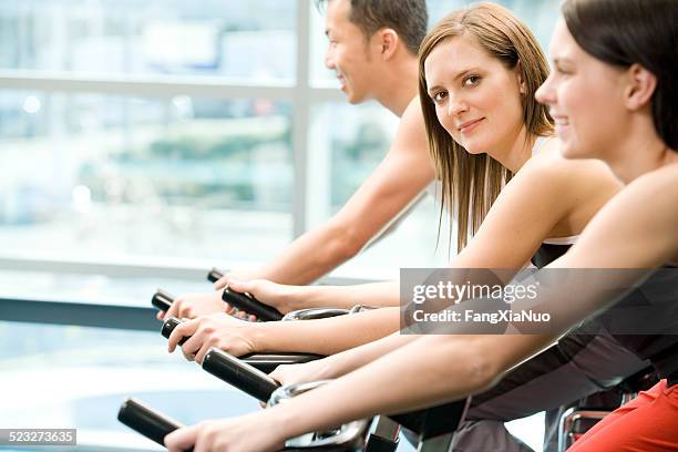 two women and a man are riding bikes at gym - surrey british columbia stock pictures, royalty-free photos & images