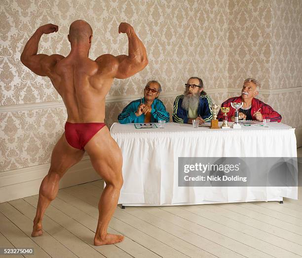bodybuilder posing for panel of senior judges - strong man stock pictures, royalty-free photos & images
