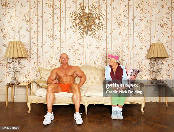 senior woman flirting with bodybuilder on sofa - body builder funny stock-fotos und bilder