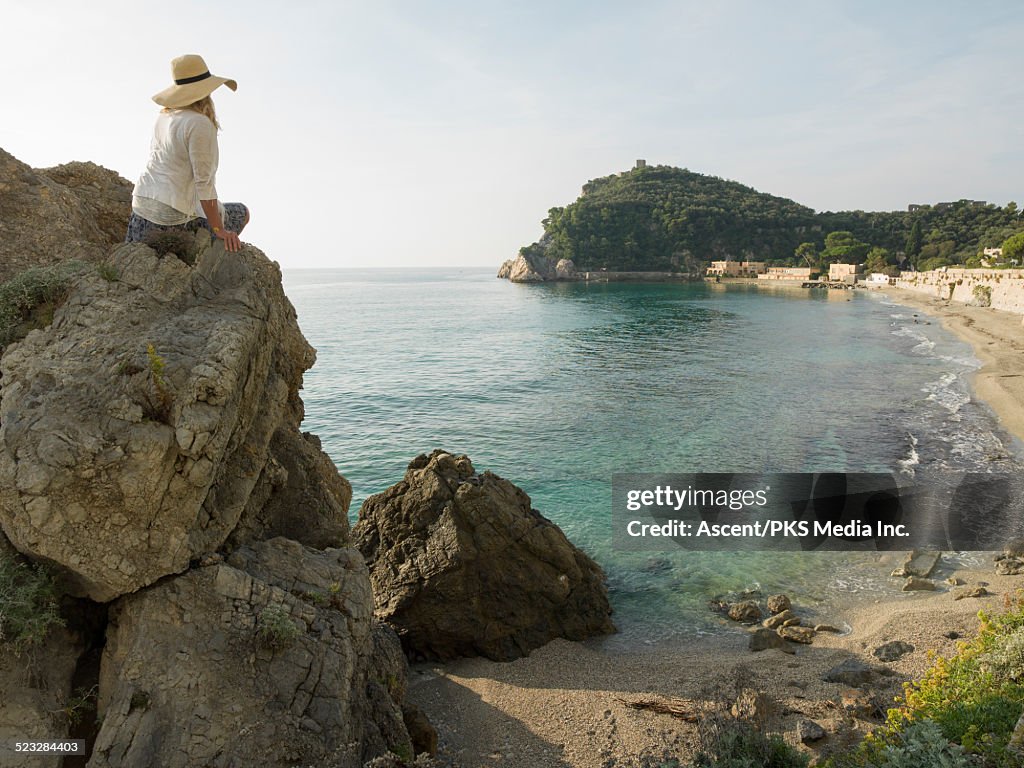 Woman relaxes on rock cliff above cove, sea