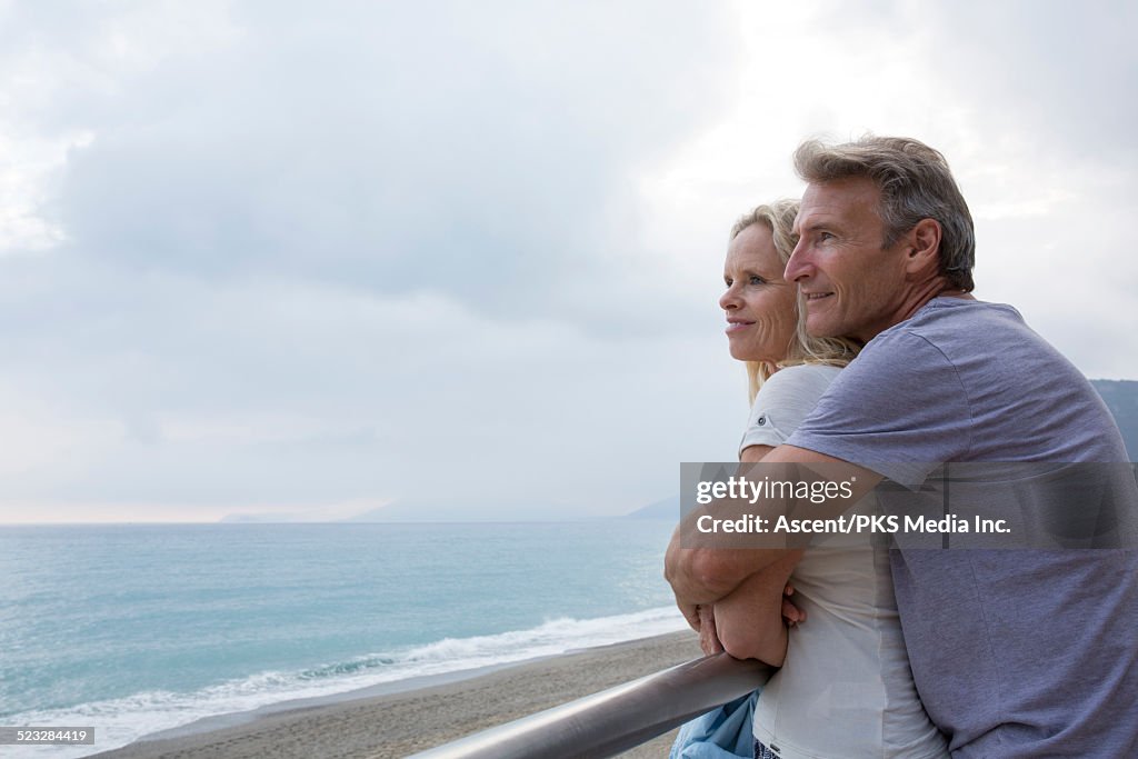 Couple embrace by railing above sea, beach