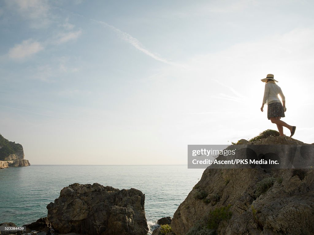 Woman ascends rock bluff above sea, sunrise