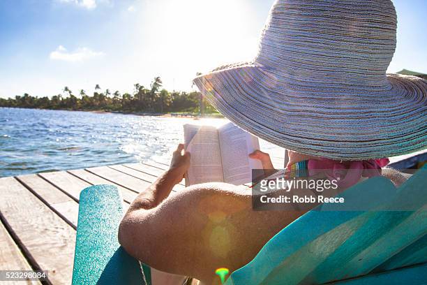 a woman on vacation in belize, sitting by the ocean reading a book - robb reece stock pictures, royalty-free photos & images