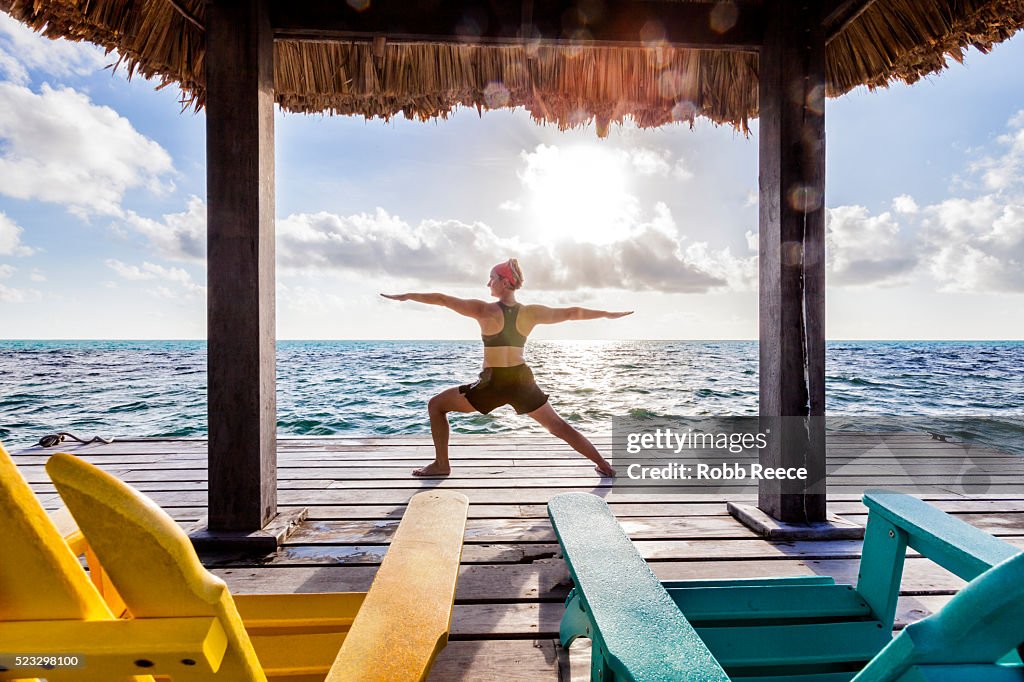 A woman on vacation in Belize, doing yoga poses on a dock near the ocean