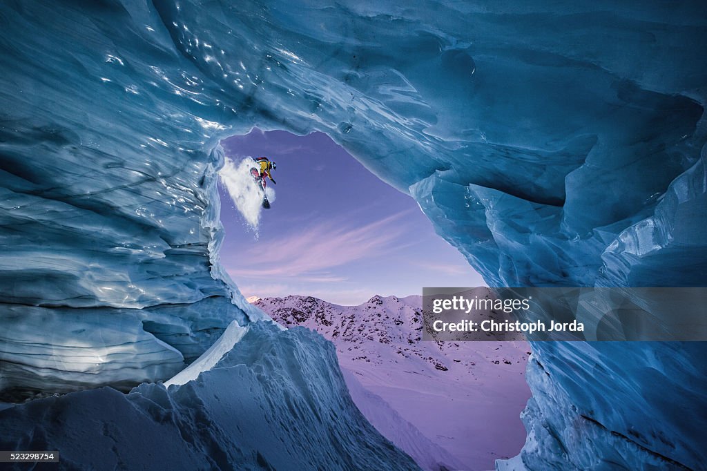 Snowboarder jumping down from a glacier cave