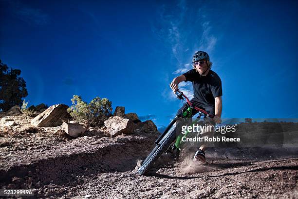 a male mountain bike rider speeds around a steep, dirt curve on a single track trail - robb reece stock pictures, royalty-free photos & images