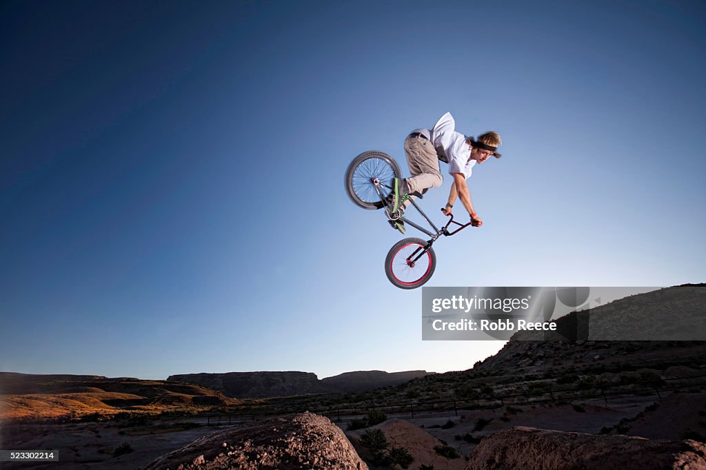 A teen boy riding and jumping his BMX bicycle over dirt hills