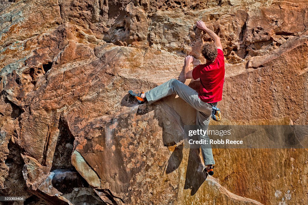 A rock climber climbing up a sandstone boulder