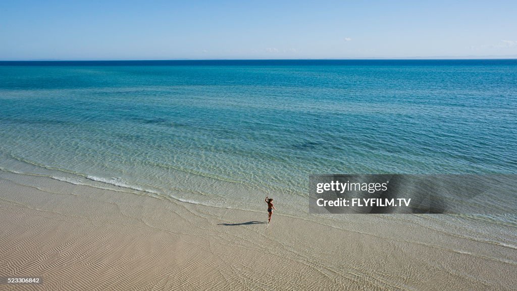 Wide aerial shot of nondescript girl jumping on beach