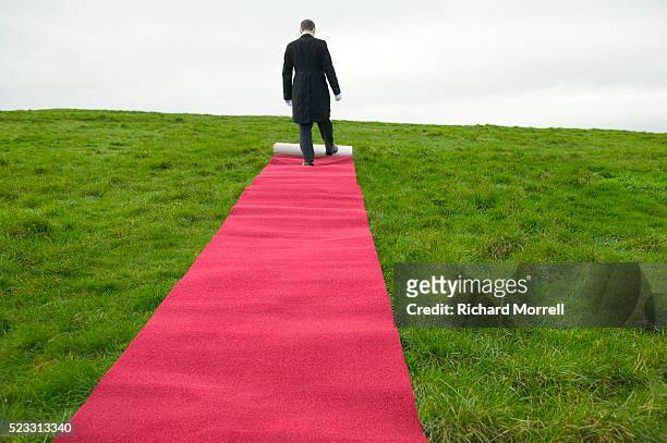 butler unrolling red carpet across field - alfombra roja fotografías e imágenes de stock