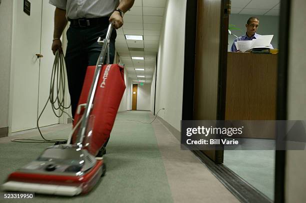 janitor vacuuming while businessman files paperwork - hauswart stock-fotos und bilder