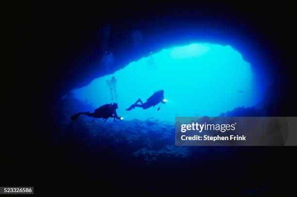 scuba divers exploring a cave opening - spelunking stock-fotos und bilder