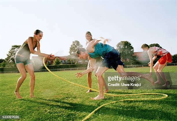 group of young people having water fight on lawn - water sprayer stock-fotos und bilder