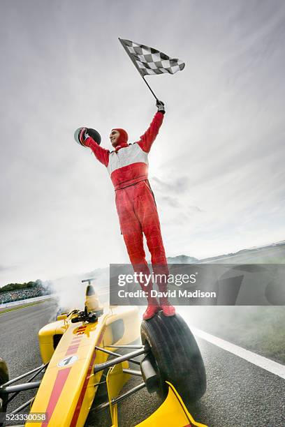 driver standing on racecar holding checkered flag - racing car driver stock pictures, royalty-free photos & images