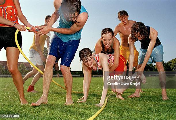 group of young people having water fight on lawn - water sprayer stock-fotos und bilder
