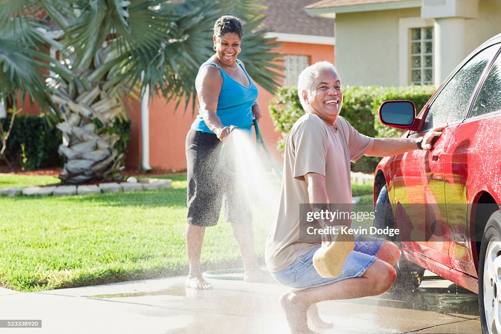 Wife spraying husband with garden hose