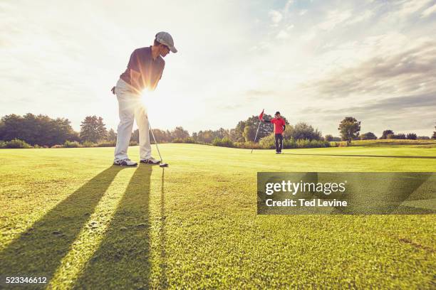 mid-adult men playing golf at sunset - golf fotografías e imágenes de stock