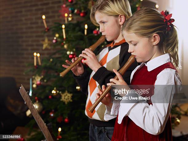 girl and boy playing recorder in front of christmas tree - blockflöte stock-fotos und bilder