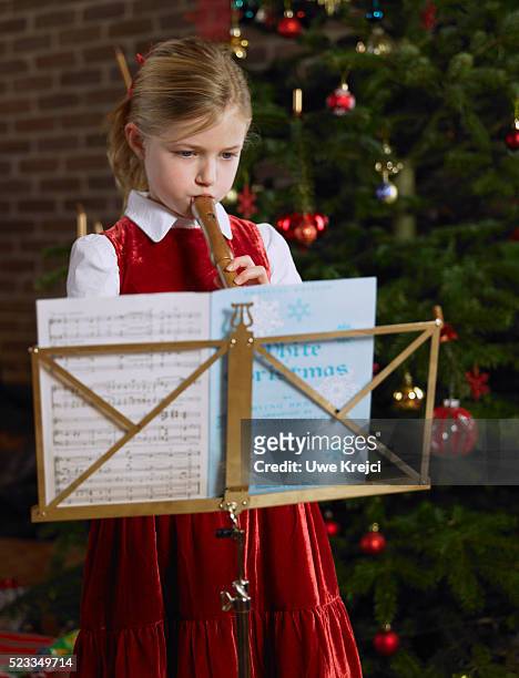 girl playing recorder in front of christmas tree - blockflöte stock-fotos und bilder